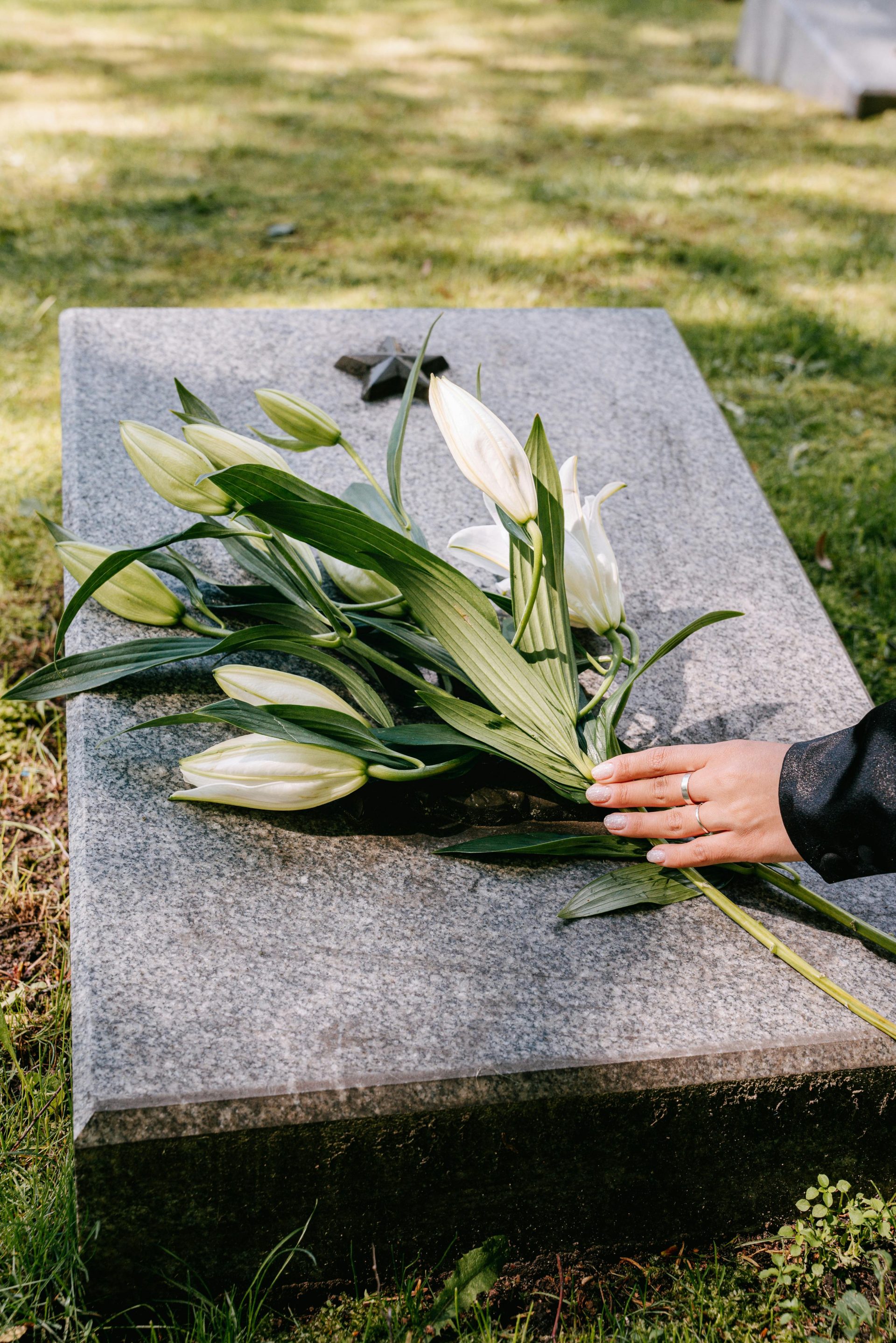 White lilies on a gravestone symbolize remembrance in an outdoor cemetery setting.