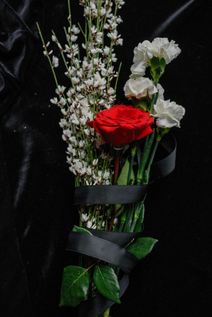 A moody bouquet featuring red and white flowers symbolizing loss on a black fabric background.