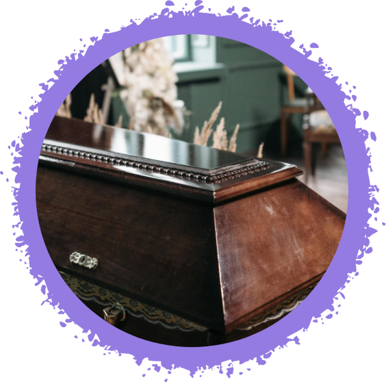A close-up shot of a polished, dark brown wooden casket, featuring decorative trim along the top edge, in a softly lit, indoor setting.